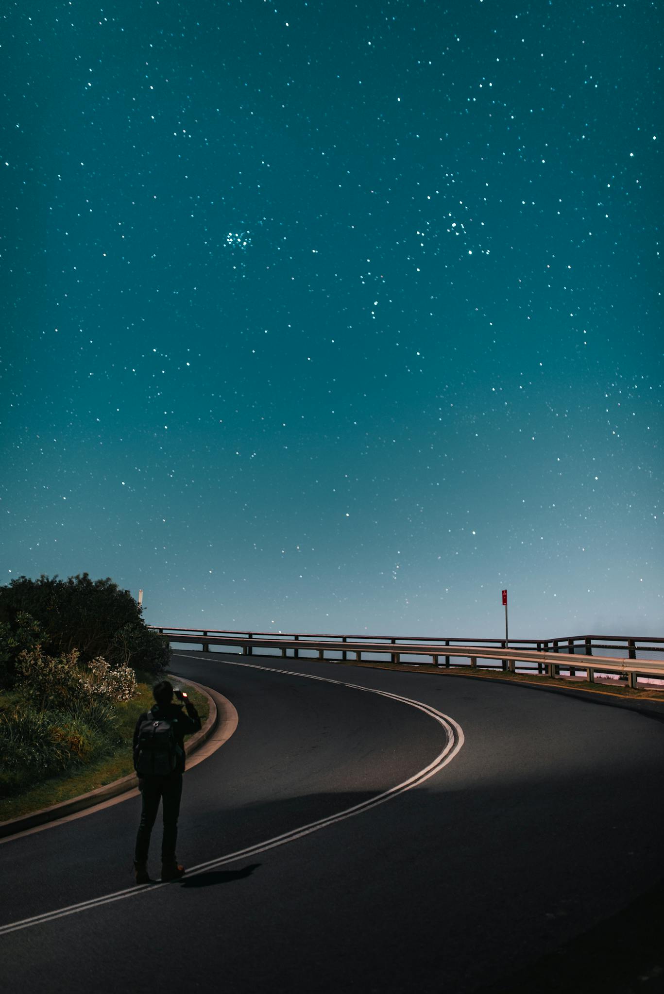 Anonymous tourist taking photo of starry sky while standing on road