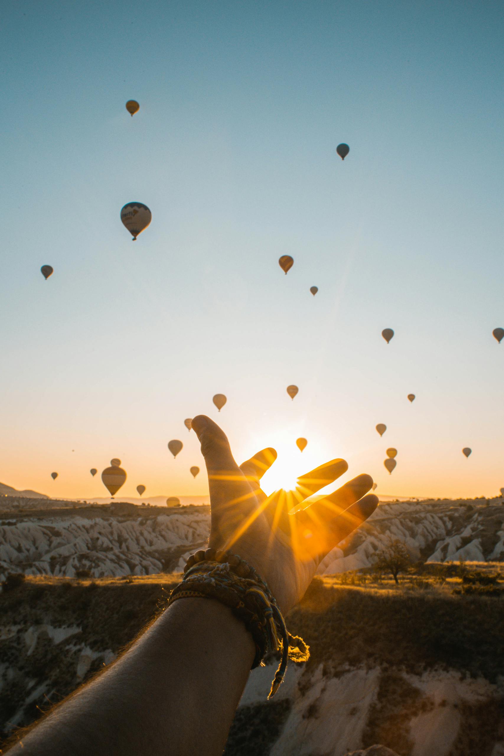 Photo of Person's Hand Across Flying Hot Air Balloons During Golden Hour